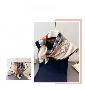 Detailed close-up of a square floral silk scarf with warm orange and grey floral patterns