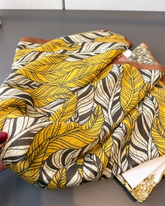 Close-up of herringbone silk scarf with yellow and black feather patterns and brown edges