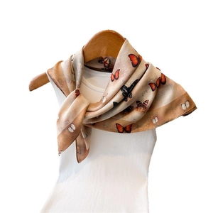 Double-sided butterfly print silk scarf in light beige hung on a wooden hanger