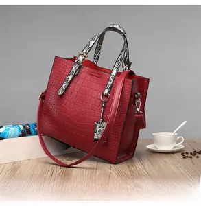 Detail of red crocodile pattern handbag with snake skin texture straps on wooden desk