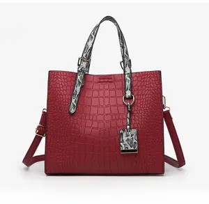 Detail of red crocodile texture tote bag with stylish snake print handles and strap