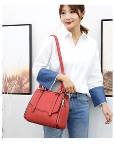 Detail of red leather crossbody bag with metal zippers shown styled with white shirt and jeans