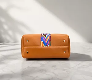 Detail view of brown leather bag bottom with golden metal feet and colorful woven strap