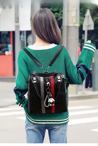Detail of black faux leather backpack featuring contrast stripes and panda charm on a model