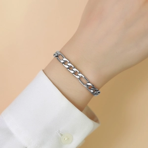 Bracelet chaîne Figaro en argent poli porté au poignet sur un poignet de chemise