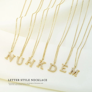 Détail de colliers alphabet dorés avec zircons brillants sur tissu blanc doux