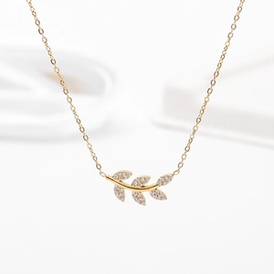 Gros plan du collier pendentif feuille dorée serti de zircons et sa fine chaîne croisée