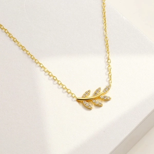 Détail du pendentif branche d'olivier dorée avec zircons brillants sur boîte cadeau blanche
