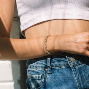 Gros plan d'un bracelet de tennis doré avec zircons ronds porté sur un poignet