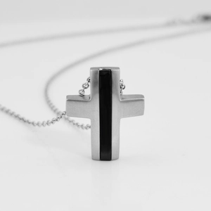 Macro shot of silver metal cross necklace with black inlay and refined texture