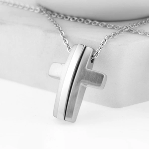 Detail of silver cross necklace showing brushed metal texture and mirror finish contrast