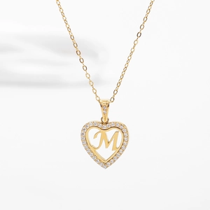 Détail macro d'un pendentif cœur doré avec lettre M et cristaux sur chaîne fine