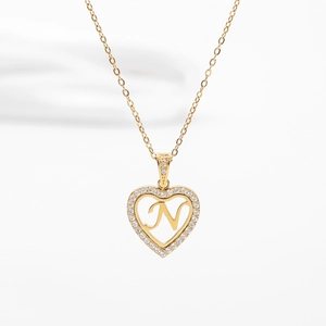 Détail de collier pendentif cœur doré avec pavé de pierres et lettre N ajourée élégante