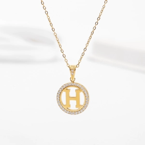 Close-up of gold-plated circular necklace pendant with letter H and crystal pavé setting