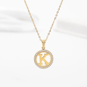 Detailed view of a gold hollow round pendant featuring letter K and pavé zircon border