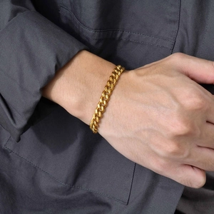 Close-up of a men's gold Cuban link chain bracelet worn on a wrist over a grey shirt