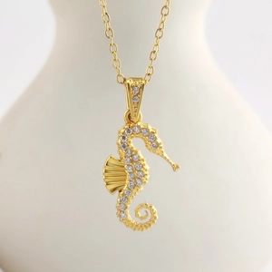 Detailed view of a golden seahorse pendant necklace with white crystals on a white bust