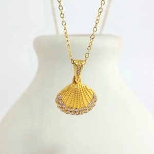 Macro detail of gold scallop shell pendant with crystals on a white ceramic vase