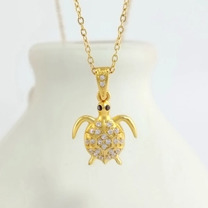 Detail view of a gold turtle pendant necklace with sparkling cubic zirconia on a white bottle