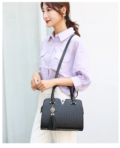 Detail of black crocodile texture handbag with metal V buckle and tassel on a model