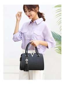 Detail of black crocodile texture handbag with silver V logo and tassel held by model
