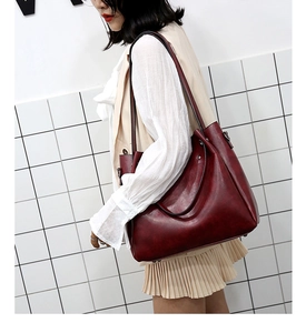 Detalle del bolso tote burdeos con asas reforzadas y textura de cuero mate usado por modelo