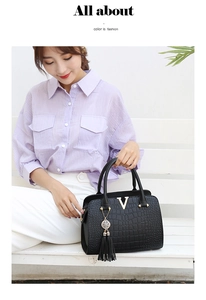 Detail of black crocodile texture handbag with gold V-buckle and tassel on model