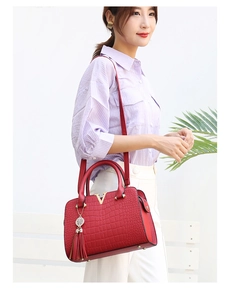 Detail of red crocodile texture handbag featuring gold V-shaped metal logo and leather tassel