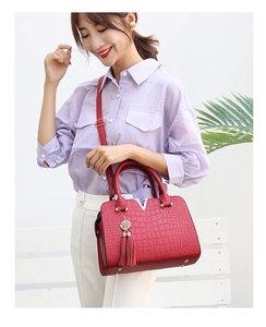 Detail view of red faux crocodile leather handbag with gold V-decoration and tassel charm