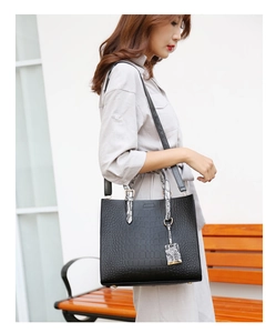 Detail of black crocodile texture handbag with snakeskin patterned handles on a bench
