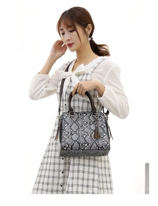Detail of grey python texture tote bag with brown tassel and top handles on model