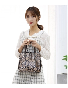 Detail of faux snake skin handbag with dark brown leather handles and tassel charm