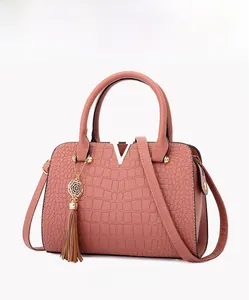 Detail view of pink crocodile pattern handbag featuring a gold V-logo and tassel