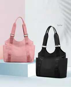 Close-up of pink and black nylon tote bags with wide shoulder straps on a geometric stand