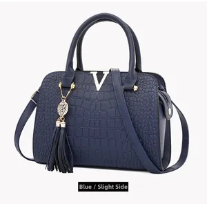 Slight side view of blue crocodile pattern handbag with gold V logo and leather tassel