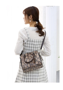 Detail of crocodile pattern handbag featuring fringe tassel and brown top handles