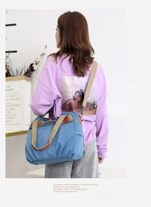 Blue canvas tote bag with adjustable shoulder strap shown being worn on a purple sweatshirt