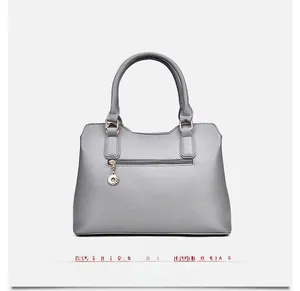 Rear view of grey leather handbag showing back zipper pocket with round metal charm