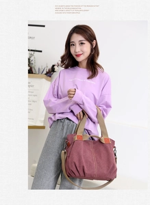 Detail of burgundy canvas tote bag with contrast handles worn by model in casual outfit
