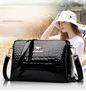 Detail of black patent leather crossbody bag with crocodile texture and gold logo