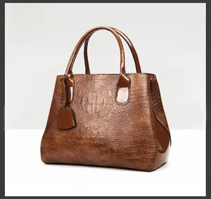 Detailed close-up of brown crocodile texture and shiny patent leather handle on a tote bag