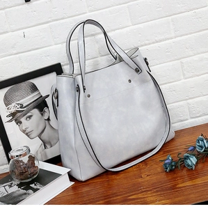 Detalle de bolso tote gris claro con tachuelas metálicas y textura de cuero en la mesa