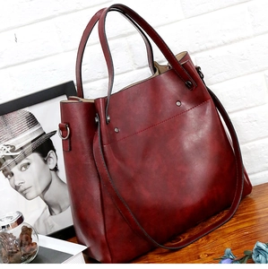 Detalle del bolso tote burdeos con textura de mármol y remaches en mesa de madera