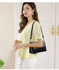 Close-up of black crocodile pattern shoulder bag on model with gold hardware detail