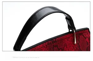 Détail d'un sac à main rouge texture serpent avec anse noire et garnitures dorées