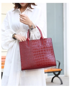 Detail of red crocodile embossed tote bag with glossy finish and gold metal feet studs