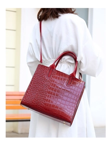Detail of burgundy crocodile-embossed tote bag worn crossbody over a white dress
