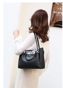Detail of black crocodile texture tote bag with snake pattern trim on shoulder strap