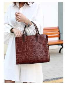 Detail of dark brown crocodile pattern tote bag with metal feet on outdoor street bench