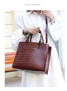 Detail of dark brown crocodile embossed tote bag featuring dual handles and metallic feet